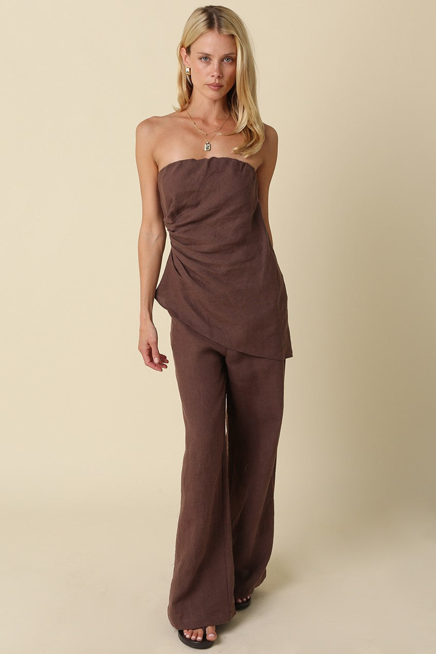 Woman wearing a brown strapless jumpsuit on a beige background