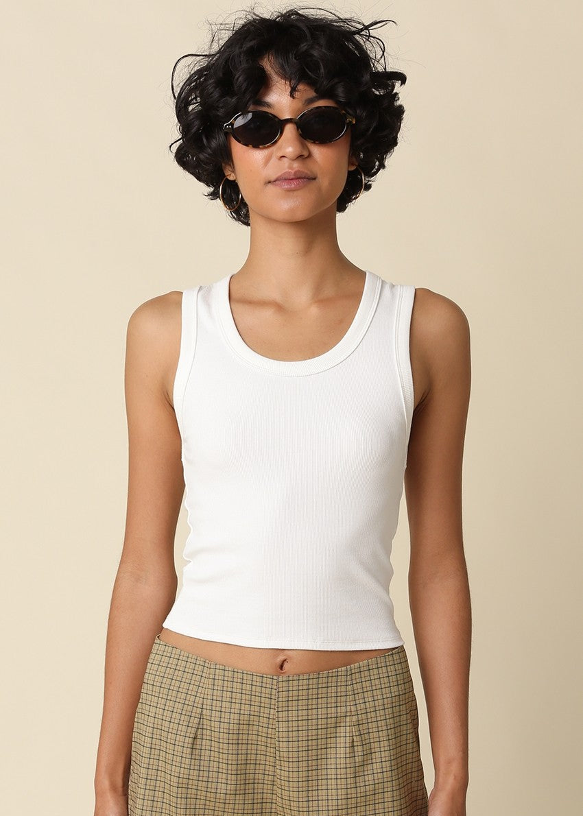 Woman wearing a white tank top and plaid pants against a beige background