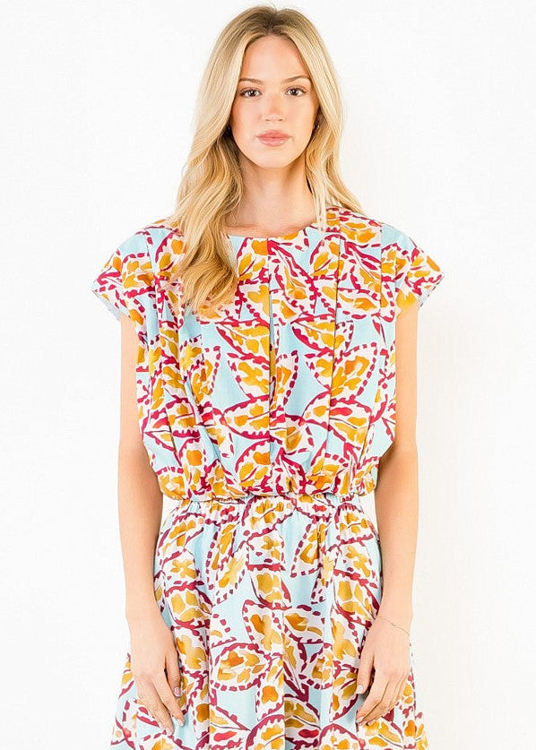 A woman modeling a short-sleeve wrap dress with a colorful abstract print on a light blue background. The dress features yellow, orange, and magenta patterns, and is photographed against a plain white studio background.