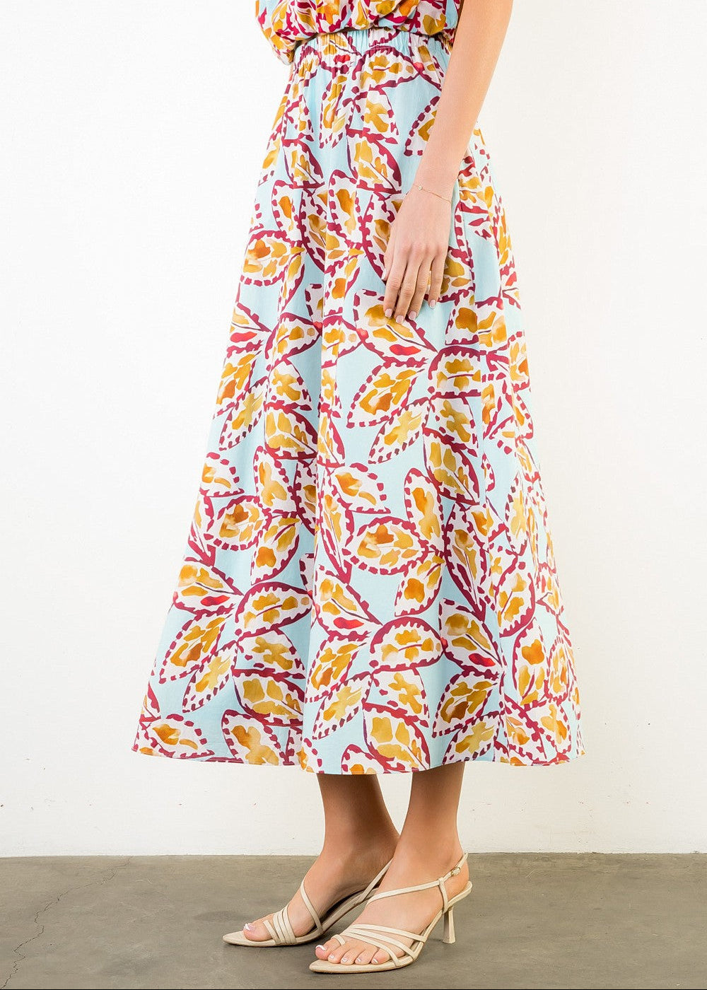 Flowy midi skirt with multicolored abstract leaf print in yellow, pink, and red on light blue background.
