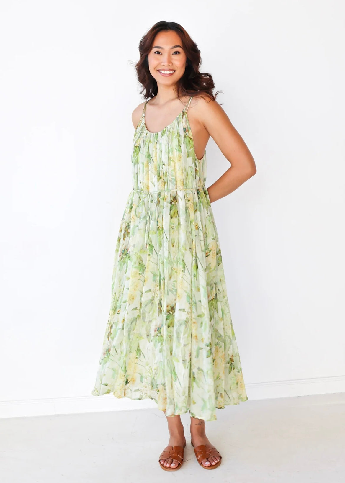 Woman wearing sleeveless maxi dress with green and yellow floral print and brown sandals.
