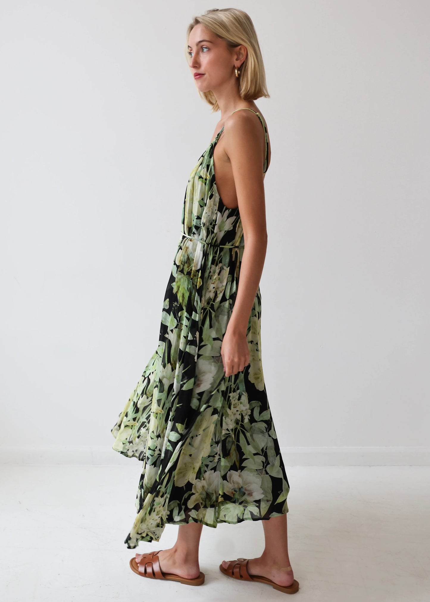 Sleeveless maxi dress with black and green floral print, V-neckline, and layered skirt on model wearing brown sandals.