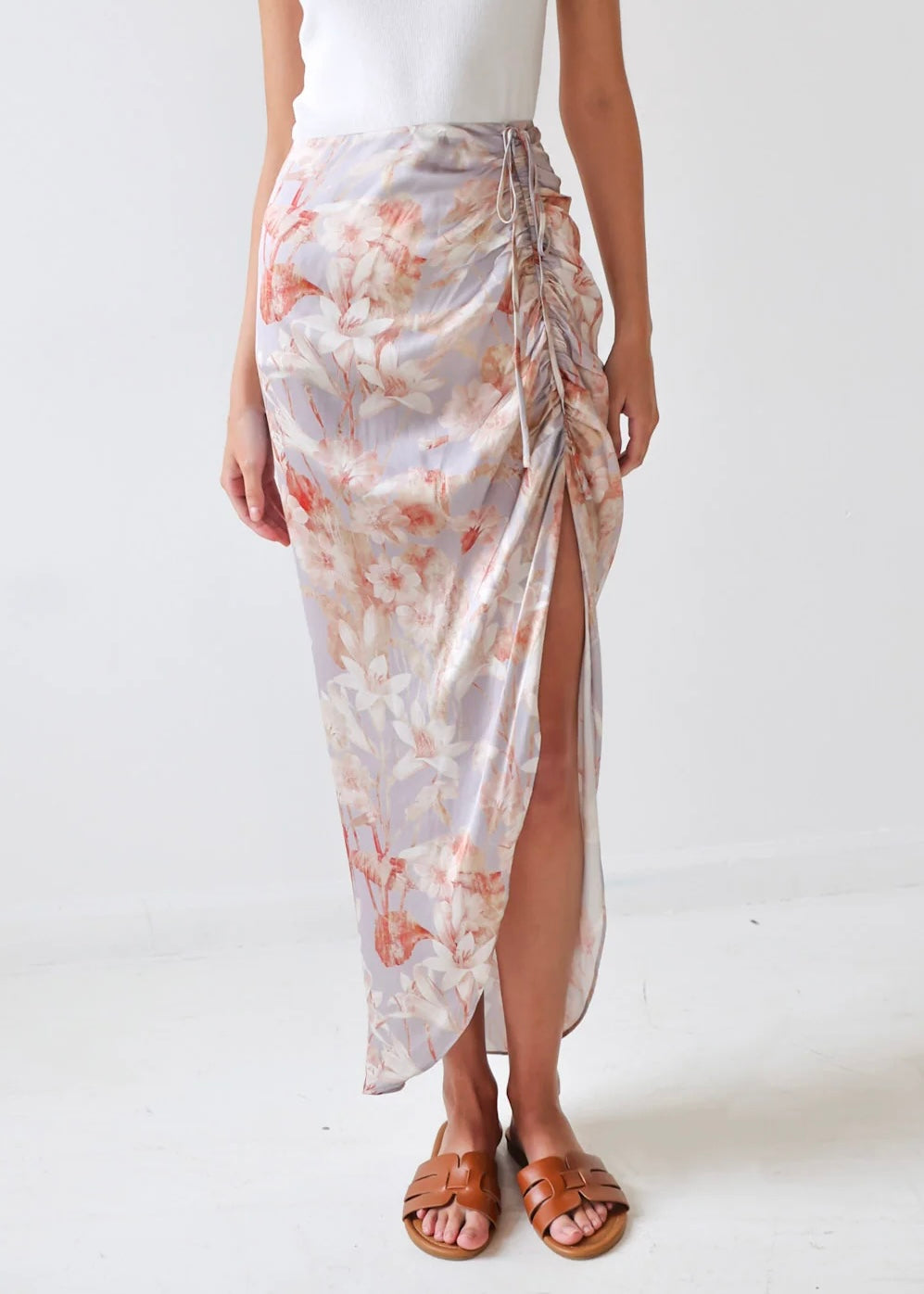 Wrap skirt with pink and coral floral print, side tie closure, and high slit, worn with white tank top and tan sandals.