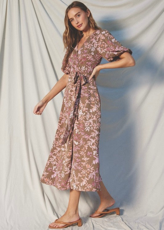 A woman models a midi wrap dress with a brown and pink floral pattern, featuring short puff sleeves, a V-neckline, and a self-tie belt, set against a draped white fabric backdrop.