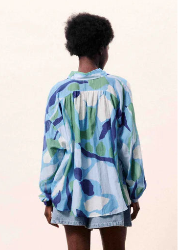 Person wearing a colorful shirt standing in front of a blue vase on a beige surface.
