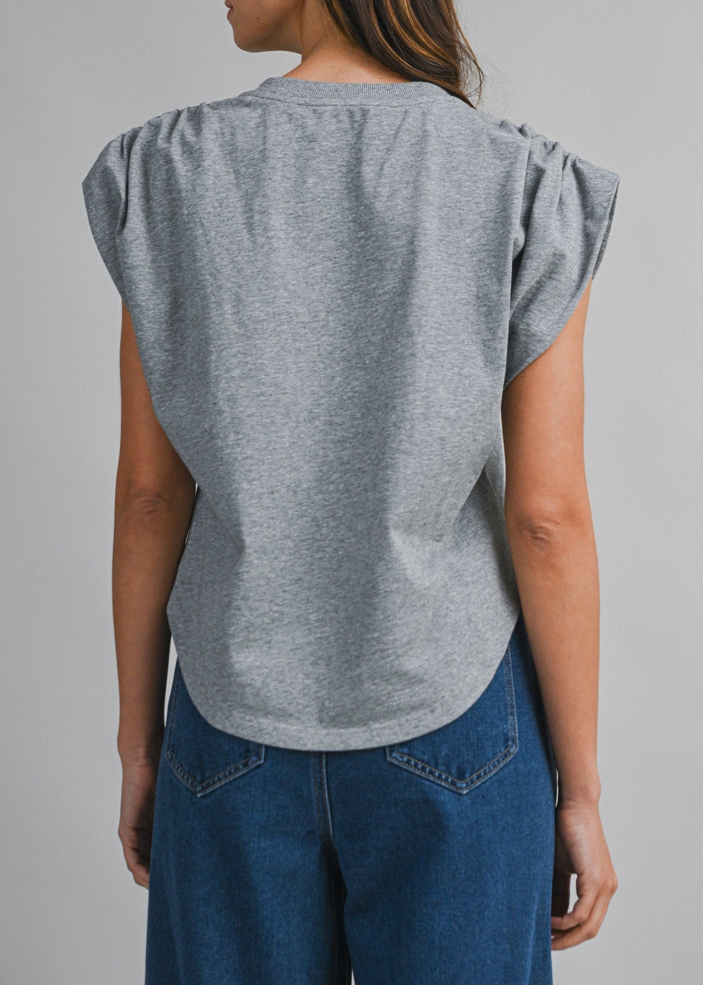 A woman shown from the back wearing a heather gray short-sleeve top with gathered puff sleeves and blue jeans, photographed against a plain light gray studio background.