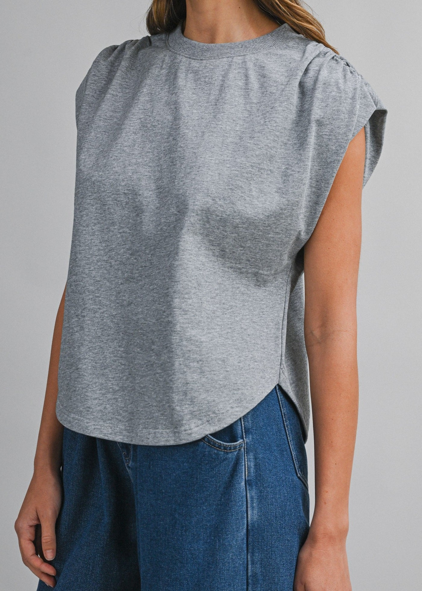 Woman wearing a gray sleeveless top and blue pants against a plain background