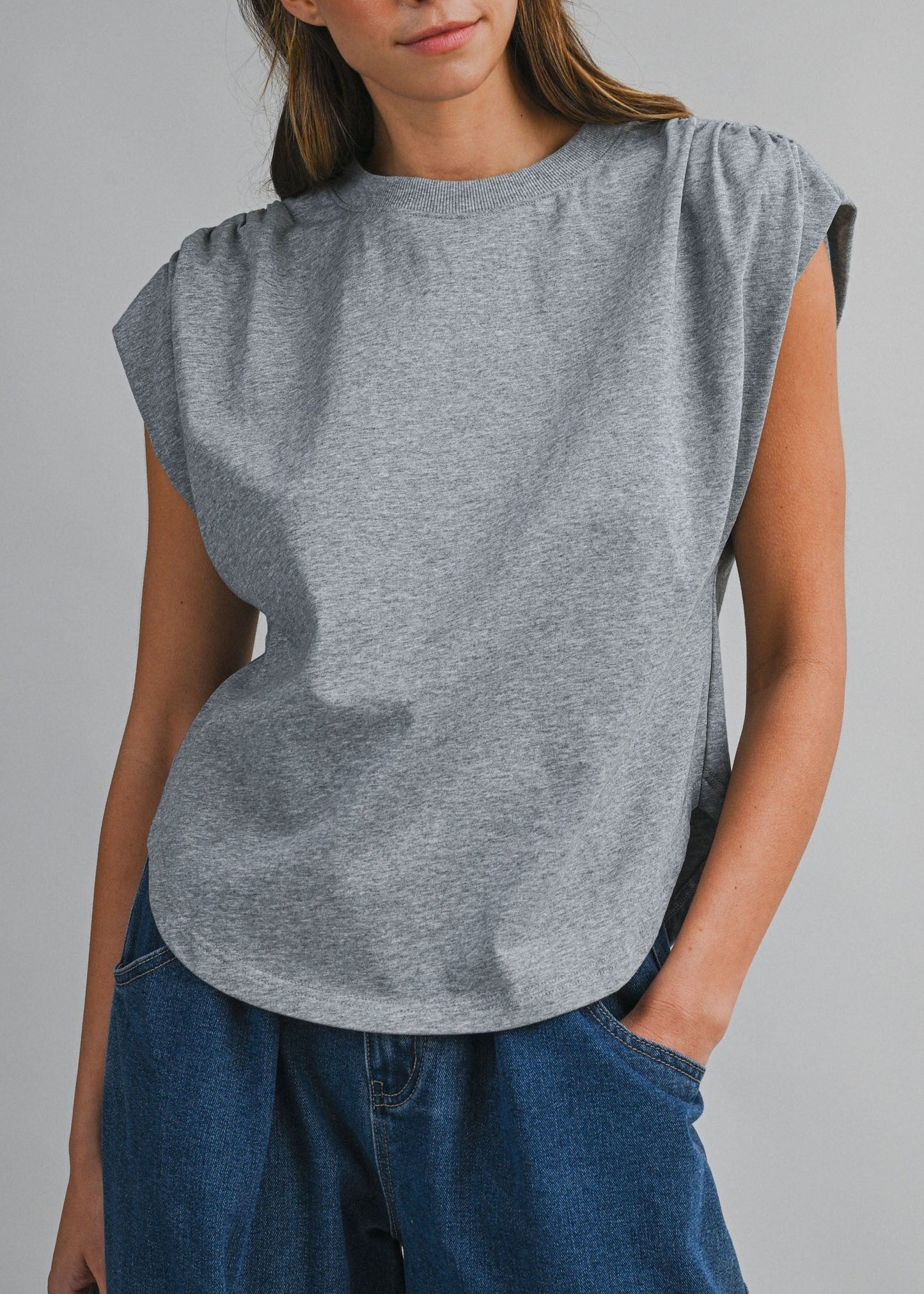 Woman wearing a gray sleeveless top and blue pants against a gray background