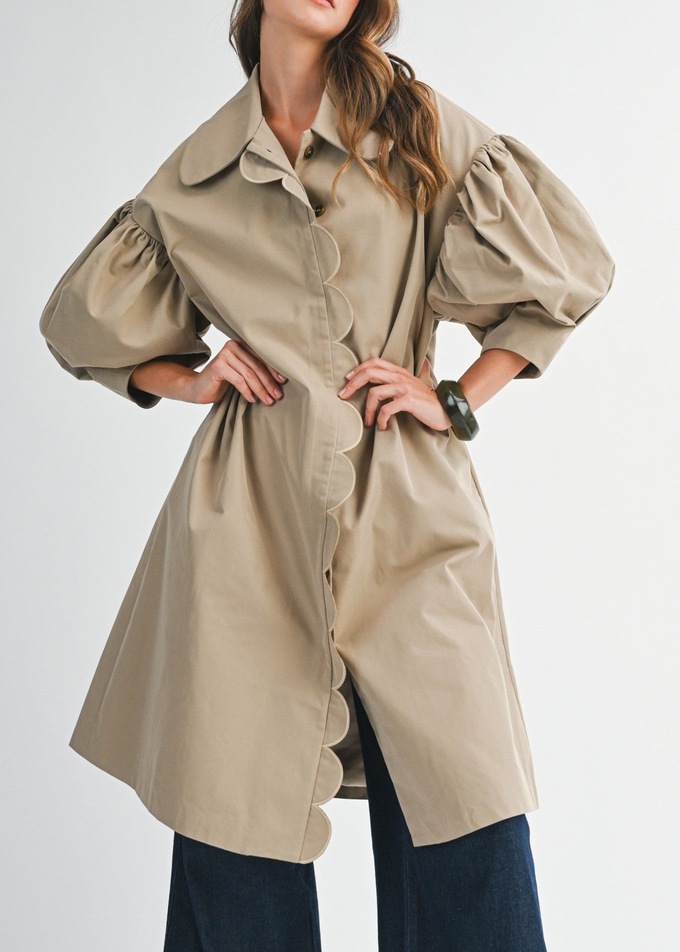 Woman wearing a beige trench coat and navy pants on a white background