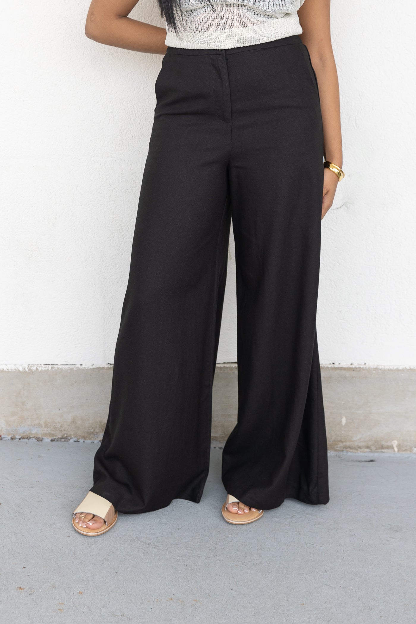Black wide-leg pants with high waist and full-length cut, styled with white knit top.