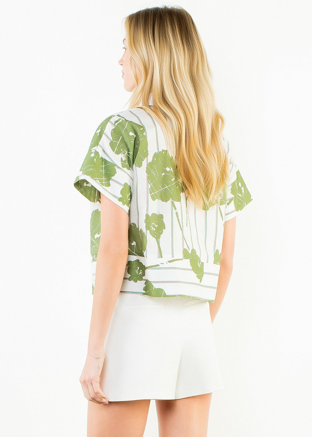 Woman wearing short sleeve top with green leaf print on white background, paired with white shorts.